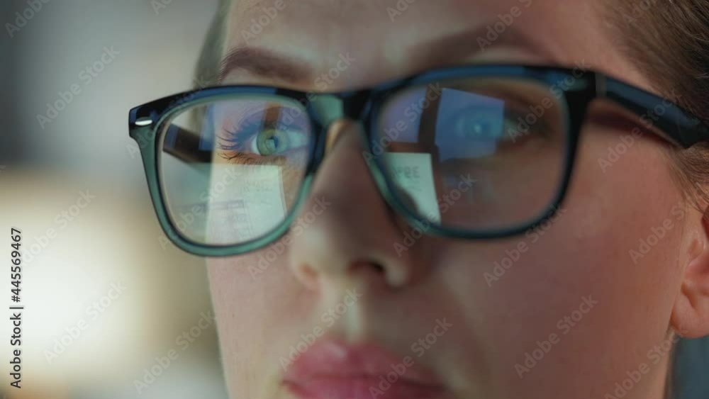 Woman in glasses looking on the monitor and and working with charts and analytics. The monitor screen is reflected in the glasses. Work at night. Extreme close-up Woman in glasses looking on the monitor and and working with charts and analytics. The monitor screen is reflected in the glasses. Work at night. Extreme close-up