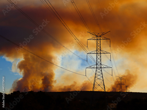 Large overland power lines leading toward the blue mountains with bush fire smoke haze across the setting sun.