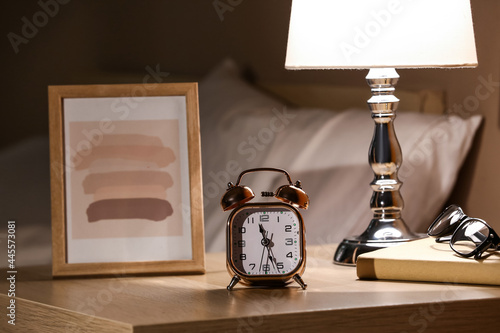 Alarm clock with picture and eyeglasses on table in bedroom at night