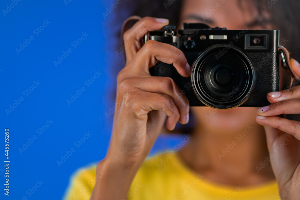 Young african american woman takes pictures with DSLR camera on blue background in studio. Girl smiling as photographer. Young african american woman takes pictures with DSLR camera on blue background in studio. Girl smiling as photographer.