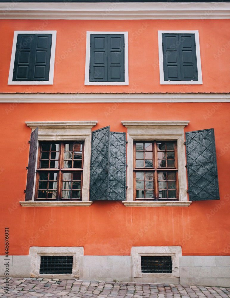 Open metal shutters on the old beautiful windows. Orange facade of the building of the Armenian courtyard in Lviv. Open metal shutters on the old beautiful windows. Orange facade of the building of the Armenian courtyard in Lviv.