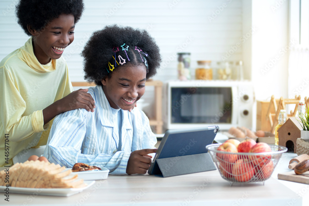 Happy African boy and older sister using a tablet computers in kitchen and smile together