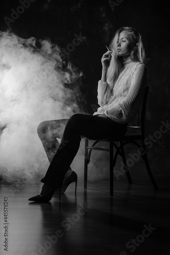 A girl in a white blouse is sitting on a chair with a cigarette in her hands, there is smoke around. Depression, feminism, loneliness, strong woman, independent, thoughts, reflections, bad habits