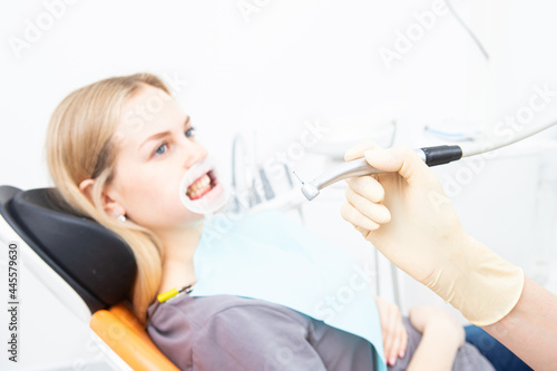 Dentist's hand with a drill on the background of a patient with a retractor in the dentist's office