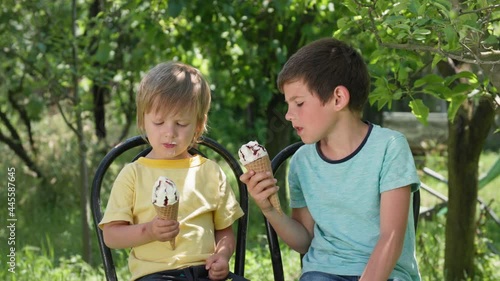 happy male children are happy to lick delicious ice cream on hot summer denm while sitting on steels background of trees photo