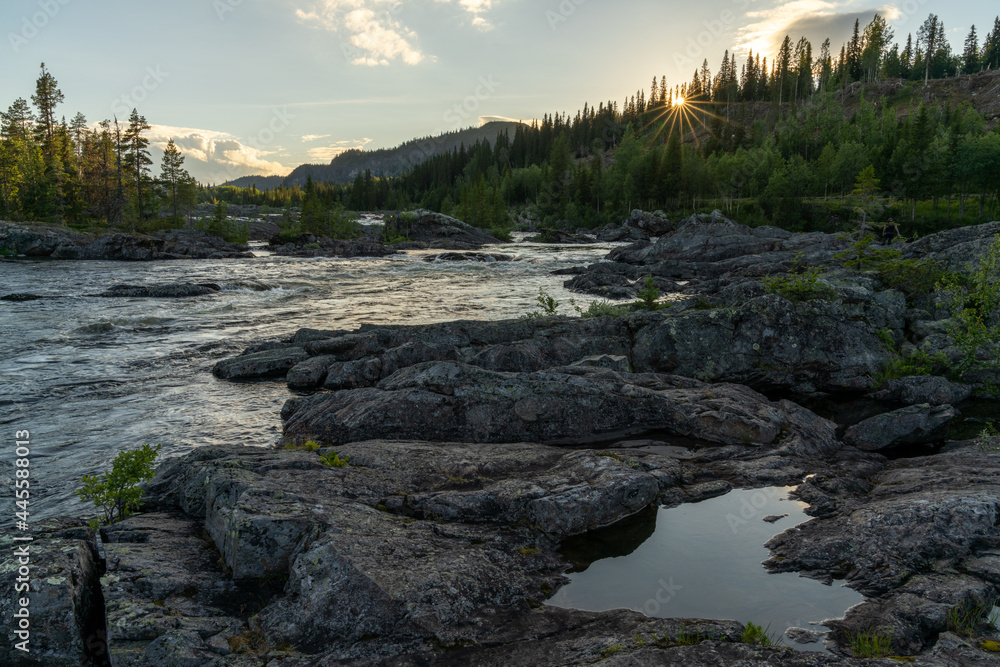 idyllic river and pine forest landscpe with a setting sun and sun star and a heart-shaped pool in the foreground