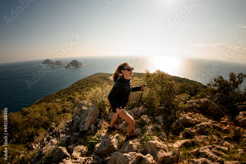 panoramic view of woman with hiking poles walking along the trail at seascape background © fesenko