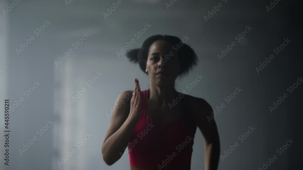 Sporty girl jogging in gym. Woman running fast in dark corridor of loft building Sporty girl jogging in gym. Woman running fast in dark corridor of loft building