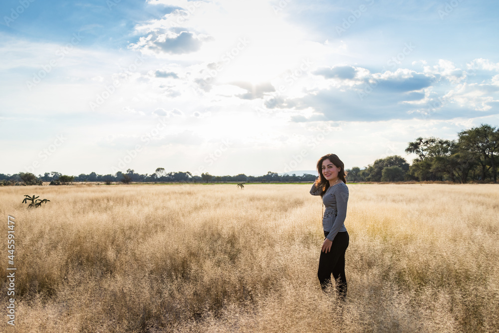 Young adult smiling Mexican woman standing in a dry grassy meadow looking at the camera Young adult smiling Mexican woman standing in a dry grassy meadow looking at the camera