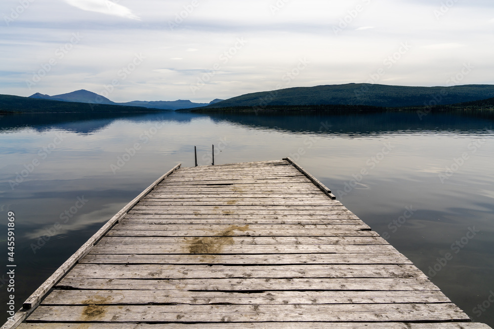 calm lake with reflections of mountains and sky and a wooden dock in the foreground