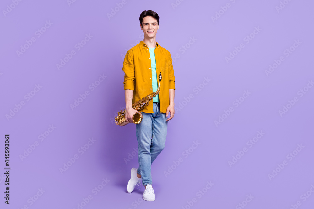 Full length photo of young man happy positive smile hold musical instrument saxophone isolated over violet color background Full length photo of young man happy positive smile hold musical instrument saxophone isolated over violet color background
