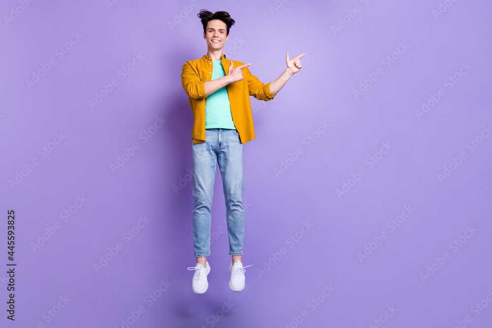 Full size photo of nice brunet millennial guy jump point empty space wear shirt jeans isolated on violet color background