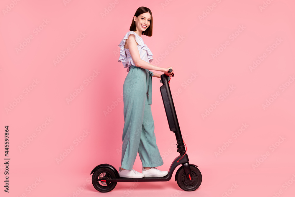 Full body profile side photo of young girl happy positive smile travel electric bike isolated over pink color background Full body profile side photo of young girl happy positive smile travel electric bike isolated over pink color background