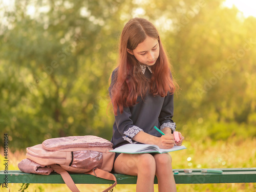 Obraz na plátně Girl teenager schoolgirl writes in a notebook sitting on a bench.