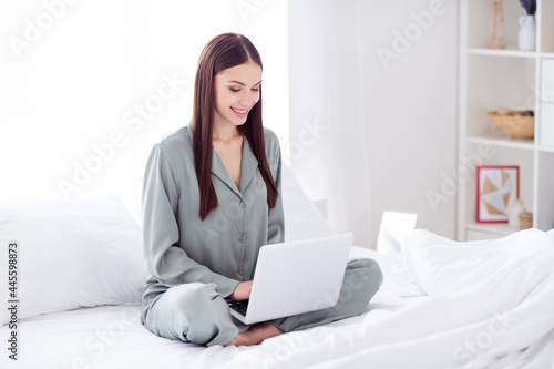 Full length body size photo woman sitting on bed wearing pajama using laptop