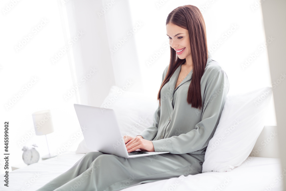 Photo of pretty sweet young lady grey sleepwear sitting bed working modern gadget smiling indoors room home house Photo of pretty sweet young lady grey sleepwear sitting bed working modern gadget smiling indoors room home house