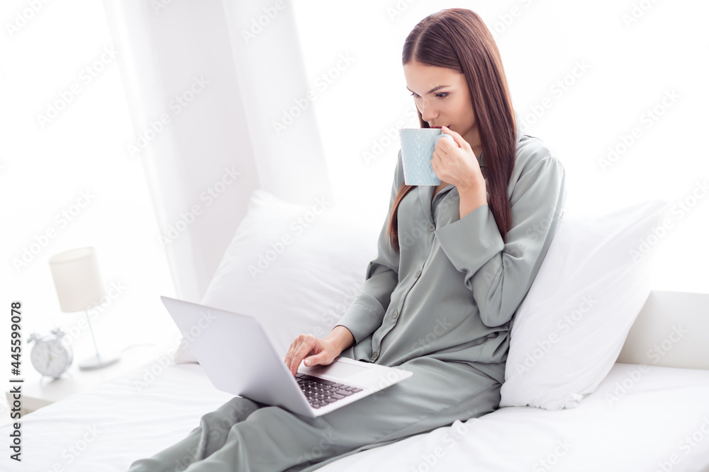 Photo of adorable cute young woman gray nightwear smiling lying bed typing modern device drinking tea indoors house home room Photo of adorable cute young woman gray nightwear smiling lying bed typing modern device drinking tea indoors house home room