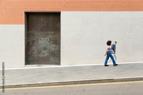 couple white man and black woman walking talking with a black iron door background with copy space