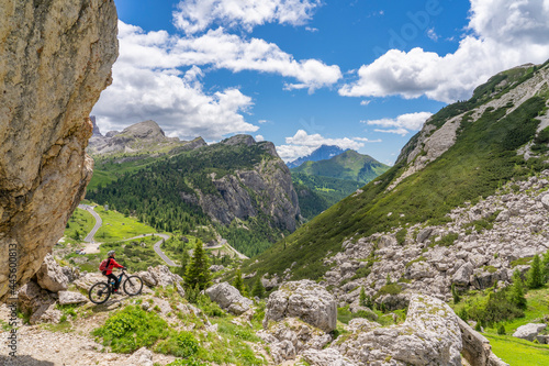 pretty active senior woman riding her electric mountain bike up to Valparola Pass  with awesome view down to Passo Falzarego in the Alta Badia Dolomites , South Tirol and Trentino, Italy photo