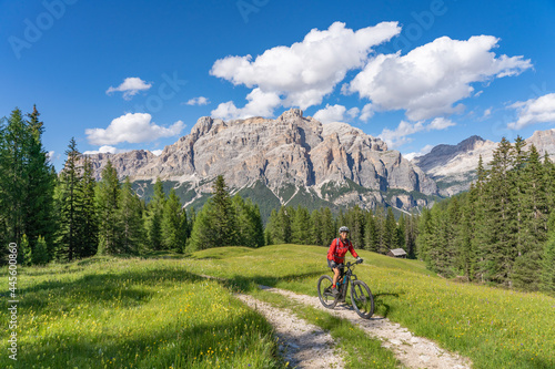 nice and active senior woman riding her electric mountain bike on the Pralongia Plateau in the Alta Badia Dolomites with awesome Sasso die Santa Cruce summit in Backg, South Tirol and Trentino, Italy