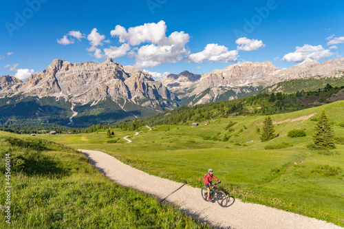 nice and active senior woman riding her electric mountain bike on the Pralongia Plateau in the Alta Badia Dolomites with awesome Sasso die Santa Cruce summit in Backg, South Tirol and Trentino, Italy