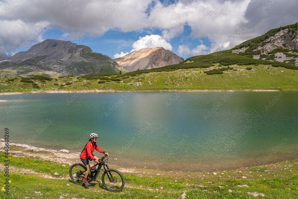 pretty active senior woman riding her electric mountain bike at Lago de in the Fanes high Valley, part of Fanes-Sennes-Braies nature park in the Alta Badia Dolomites,  South Tirol and Trentino, Italy

