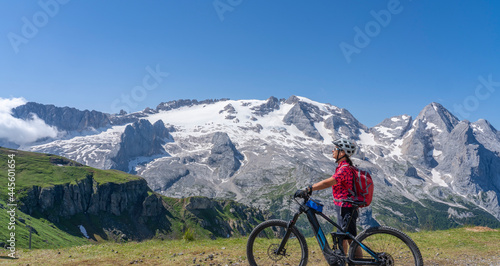 nice and active senior woman riding her electric mountain bike on the Pralongia Plateau in the Alta Badia Dolomites with glacier of Marmolata summit in Background  South Tirol and Trentino  Italy 