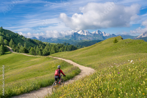nice and active senior woman riding her electric mountain bike on the Pralongia Plateau in the Alta Badia Dolomites with glacier of Marmolata summit in Background, South Tirol and Trentino, Italy 