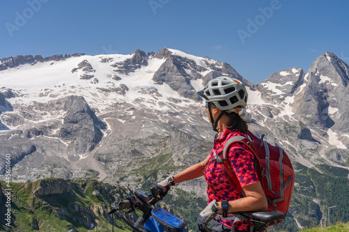 nice and active senior woman riding her electric mountain bike on the Pralongia Plateau in the Alta Badia Dolomites with glacier of Marmolata summit in Background, South Tirol and Trentino, Italy
 photo