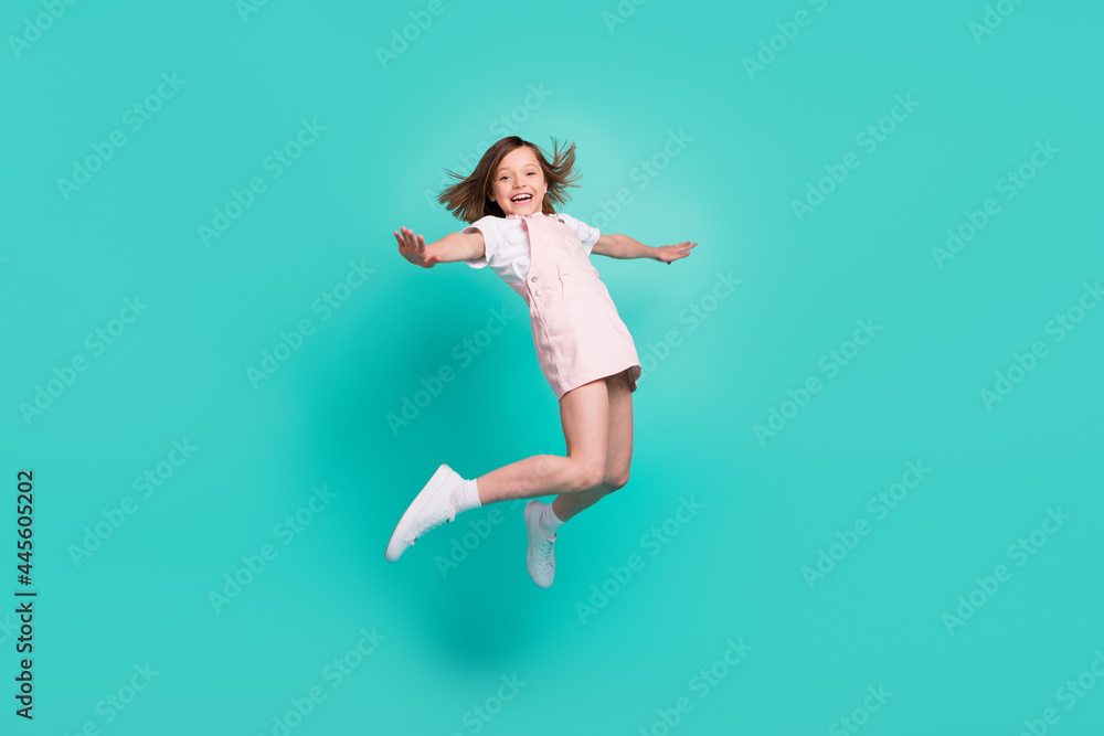 © deagreez - Photo of pretty adorable school girl wear pink overall smiling jumping high arms sides isolated teal color background © deagreez - Photo of pretty adorable school girl wear pink overall smiling jumping high arms sides isolated teal color background