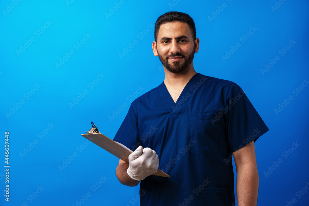 Young arab doctor holding a clipboard on a blue background Young arab doctor holding a clipboard on a blue background