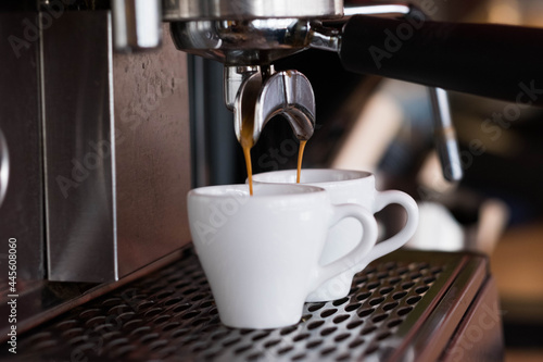 The espresso machine pours two coffees into white cups.