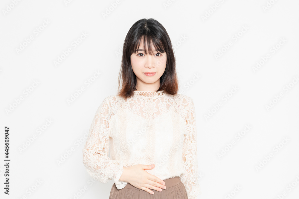 白背景の前に立って、お腹に手を当てる、レースのブラウスを着た若い女性 白背景の前に立って、お腹に手を当てる、レースのブラウスを着た若い女性