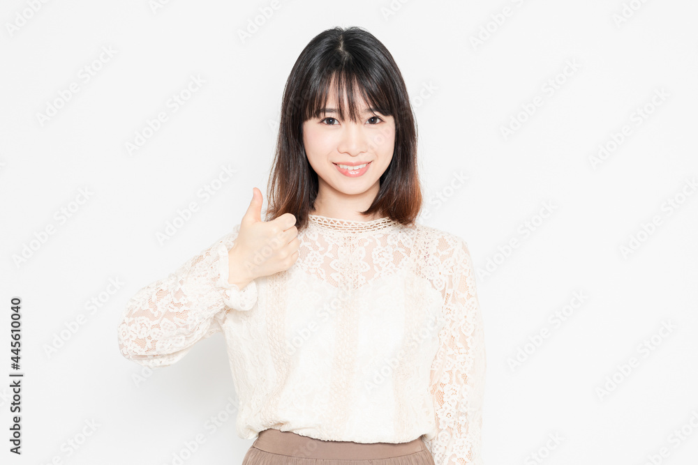白背景の前に立って、いいねのジェスチャーをする、レースのブラウスを着た若い女性 白背景の前に立って、いいねのジェスチャーをする、レースのブラウスを着た若い女性
