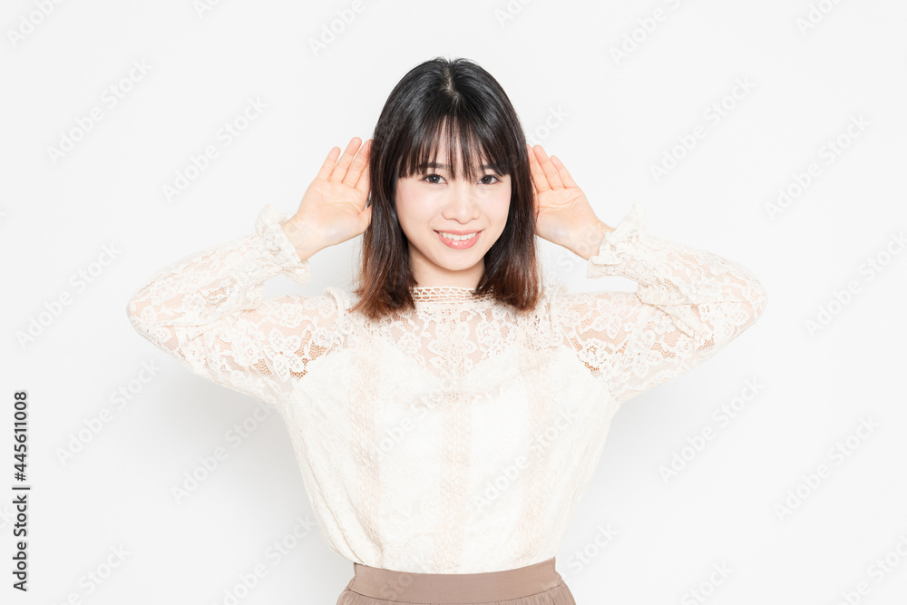 白背景の前に立って、聞き耳を立てる、レースのブラウスを着た若い女性