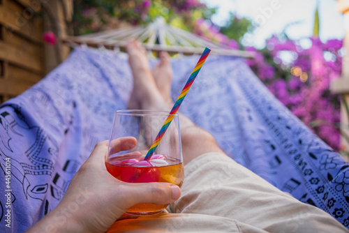 Картината върху платно Legs of a man lying in a hammock drinking a cocktail with a colorful straw