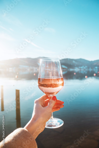 Female hand with glass of rose  wine. Cozy pier on the coast of the lake Tegernsee. Alpine mountains in Bavaria. Mountain view, beautiful landscape in Germany. Adventure in Europe.