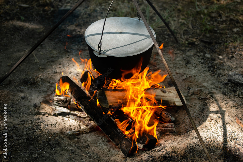 Tourists prepare lunch in hiking pot on campfire at campsite. Bowler on bonfire. Soup boils in cauldron. Tourists prepare lunch in hiking pot on campfire at campsite. Bowler on bonfire. Soup boils in cauldron.