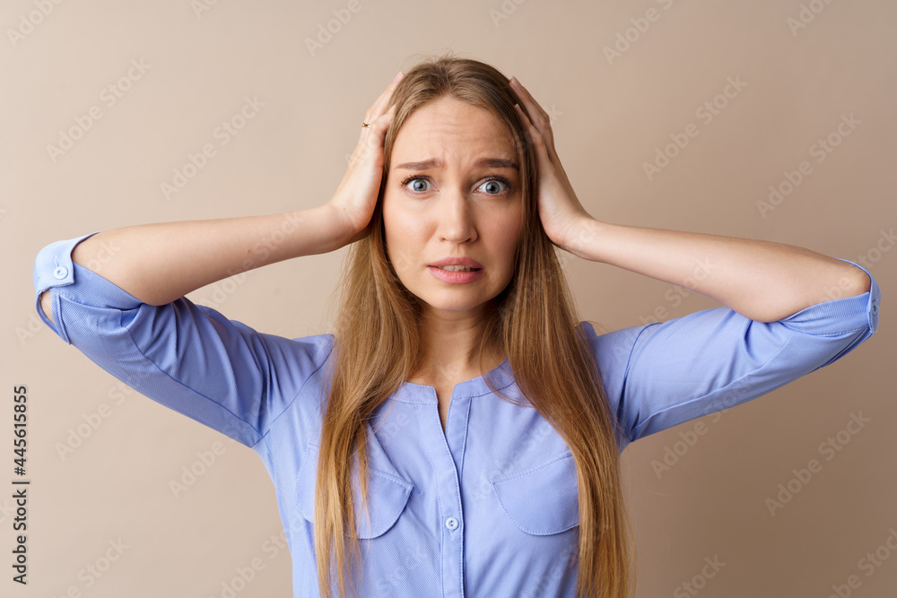 Stressed and confused young woman holding her head against beige background