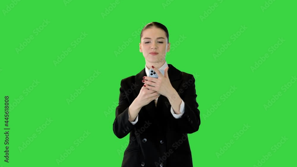 Young woman in office suit walking typing some text on her smartphone and smiling on a Green Screen, Chroma Key. Young woman in office suit walking typing some text on her smartphone and smiling on a Green Screen, Chroma Key.