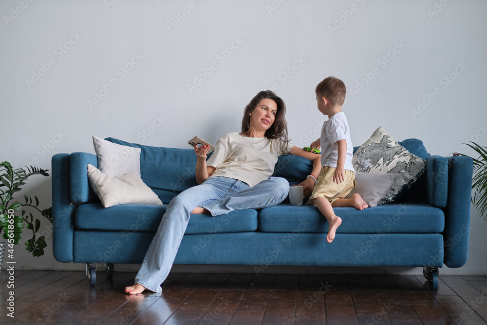 tired young mother or nanny resting on the couch wants to relax at the phone but the child needs attention