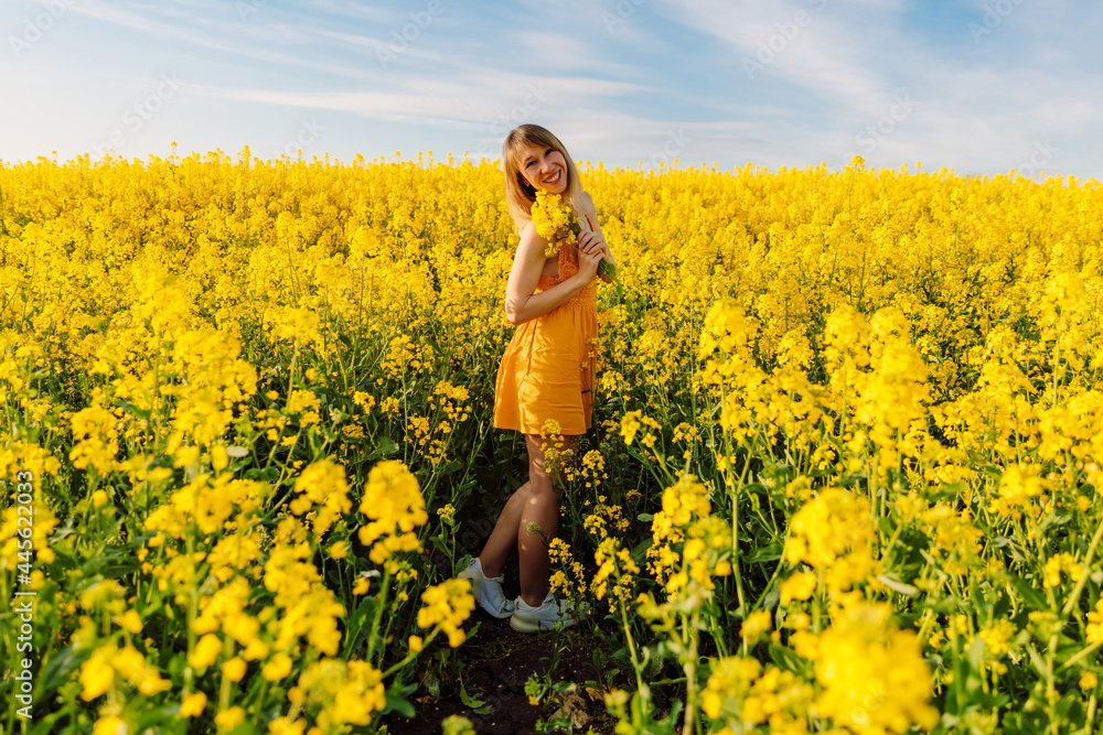 Attractive cheerful woman on rapeseed field with sunset light. Yellow flowers and caucasian woman Attractive cheerful woman on rapeseed field with sunset light. Yellow flowers and caucasian woman