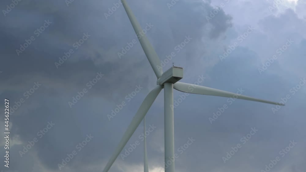 Large blades of alternative electricity source windmill rotate under sky with dense grey clouds on new wind farm low angle shot. Sustainable clean energy concept. Large blades of alternative electricity source windmill rotate under sky with dense grey clouds on new wind farm low angle shot. Sustainable clean energy concept.
