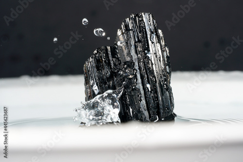 Closeup of a black tourmaline minerals with water droplets on a white surface photo