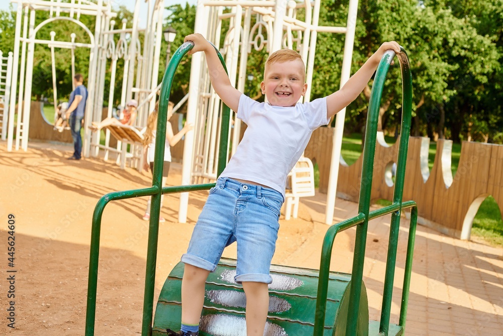 Fototapeta premium A small red-haired five-year-old boy is playing on the playground in the park in the summer