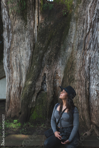 Latin girl on vacation in the magical town of Valle de Bravo, knowing its tourist places, such as the giant weeping willow, enjoys the moment while taking photos.