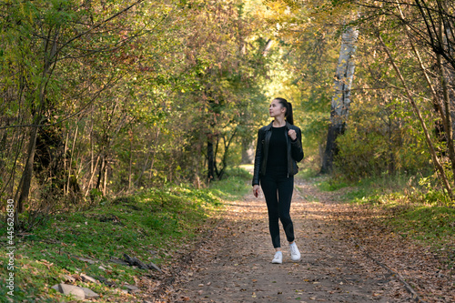 Girl walks in the autumn park. Young beautiful woman in black clothes in the forest. Alley, promenade. © somemeans