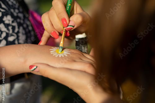 Draws a flower on her hand. The girl draws a flower to the child