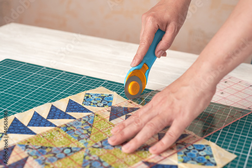 Home craft concept photo - woman hands, cutting textile for patchwork or quilt on a mat with rotary cutter and ruler.