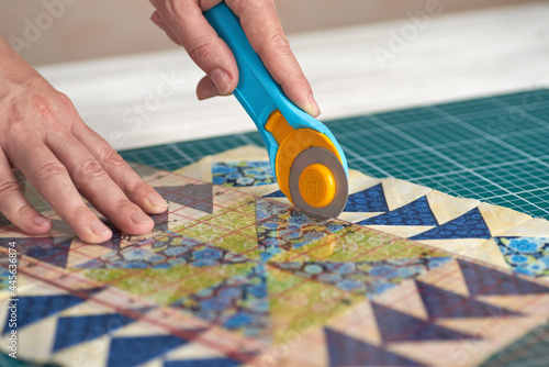 Home craft concept photo - woman hands, cutting textile for patchwork or quilt  on a mat with rotary cutter and ruler.